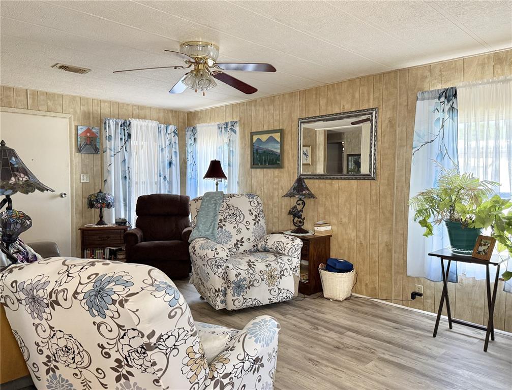 A living room features wood-paneled walls, floral-patterned armchairs, a ceiling fan, and light-colored flooring — 34642 SWEETPEA LANE LANE, ZEPHYRHILLS, FL