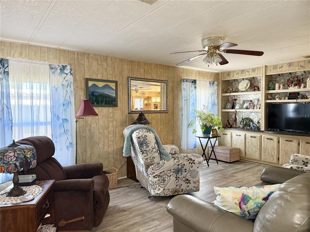 A living room features wood-paneled walls, a ceiling fan, built-in shelving, and various armchairs — 34642 SWEETPEA LANE LANE, ZEPHYRHILLS, FL