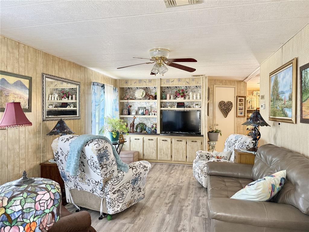 A living room features wood-paneled walls, a built-in entertainment center, and floral-patterned armchairs — 34642 SWEETPEA LANE LANE, ZEPHYRHILLS, FL