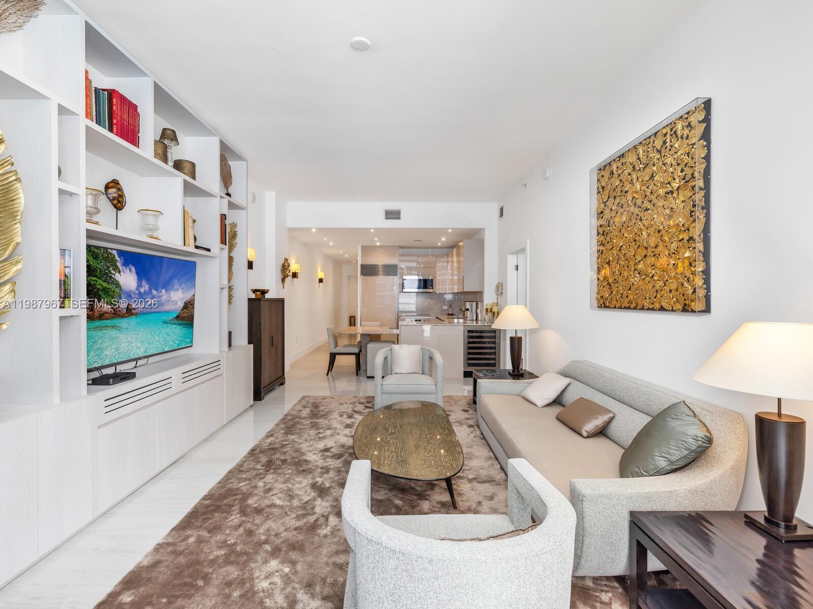 A modern living room features a large built-in media wall, neutral furniture, and gold artwork — 6799 Collins Ave # 501, Miami Beach FL 33141, MIAMI BEACH, FL