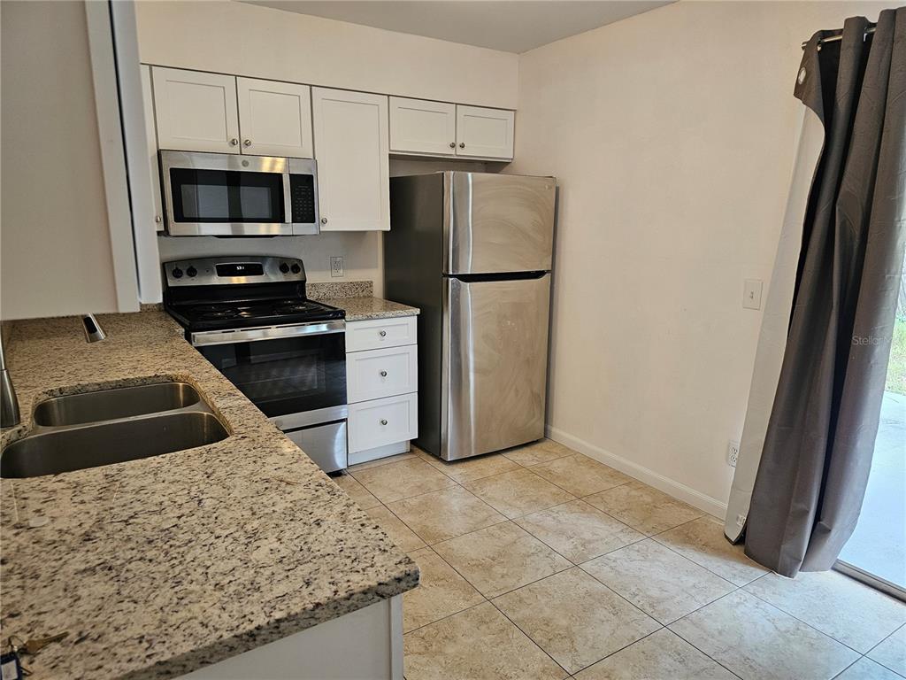 A kitchen features stainless steel appliances, white cabinets, granite countertops, and light-colored tile flooring — 7626 GOLDEN GLENN DRIVE, ORLANDO, FL