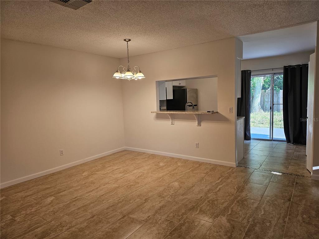 A dining area features tile flooring, a chandelier, and a pass-through window to the kitchen — 7626 GOLDEN GLENN DRIVE, ORLANDO, FL