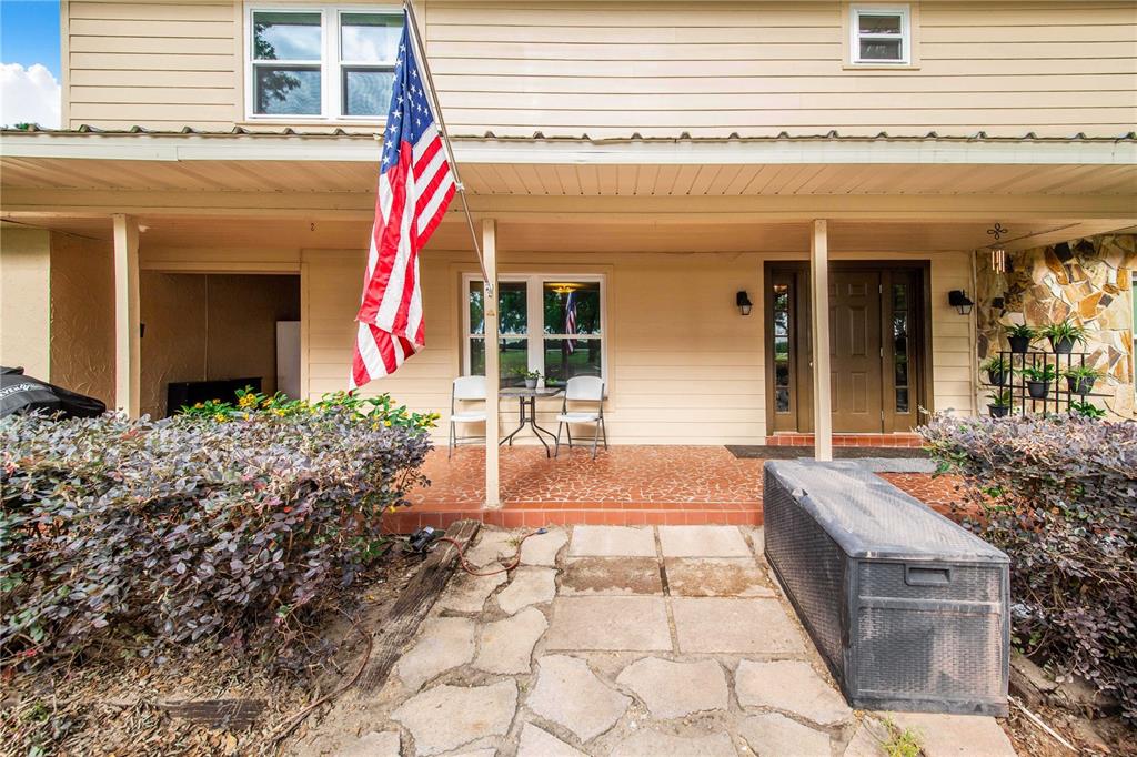 A tan house exterior features a covered porch, an American flag, and a stone walkway — 1646 TYNER ROAD, HAINES CITY, FL