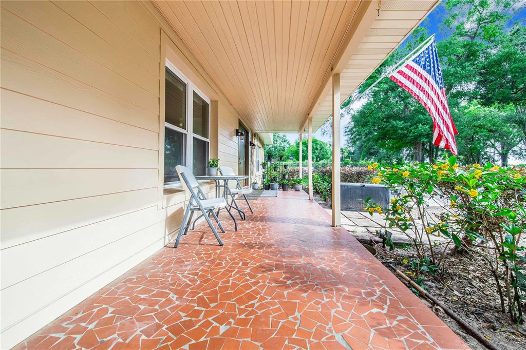 A covered porch features a red mosaic tile floor, two white chairs, and an American flag — 1646 TYNER ROAD, HAINES CITY, FL