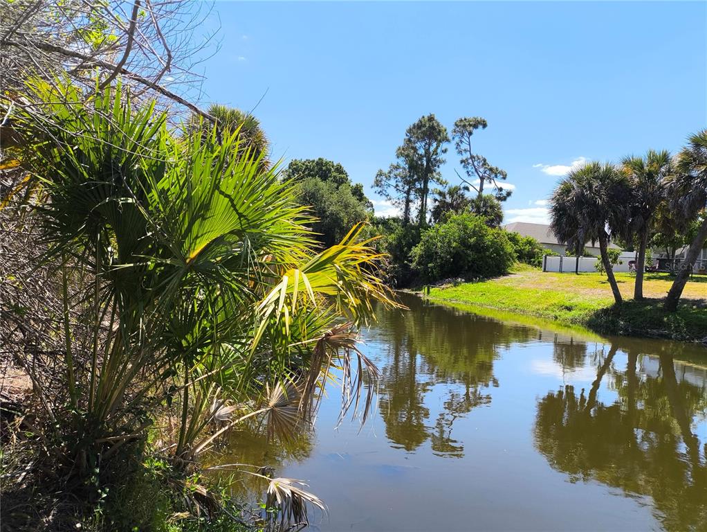 A view of a narrow canal lined with palm trees and lush vegetation — 12289 CLARENDON AVENUE, PORT CHARLOTTE, FL