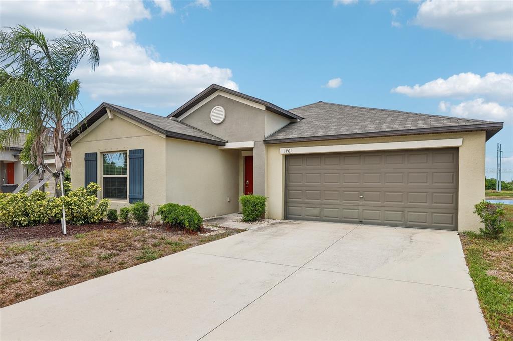 A single-story suburban house with a tan stucco exterior, a two-car garage, and a palm tree — 1461 GOLDEN GLOW DRIVE, RUSKIN, FL