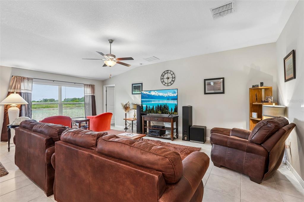 A living room features brown leather furniture, a television, and a large window with blinds — 1461 GOLDEN GLOW DRIVE, RUSKIN, FL