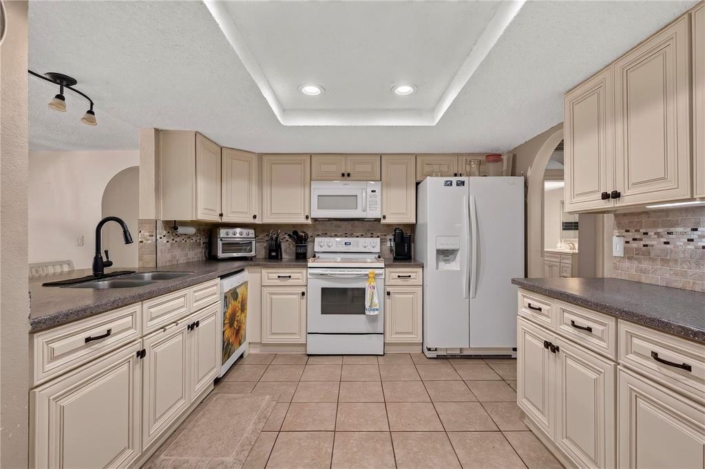 A kitchen features beige cabinets, a white refrigerator, a white stove, and tiled flooring — 13129 FILBERT STREET, HUDSON, FL