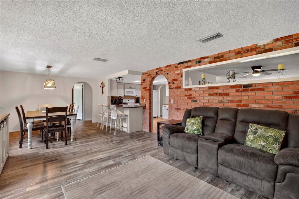 A living room with a brick accent wall, dining area, and kitchen with bar seating — 13129 FILBERT STREET, HUDSON, FL