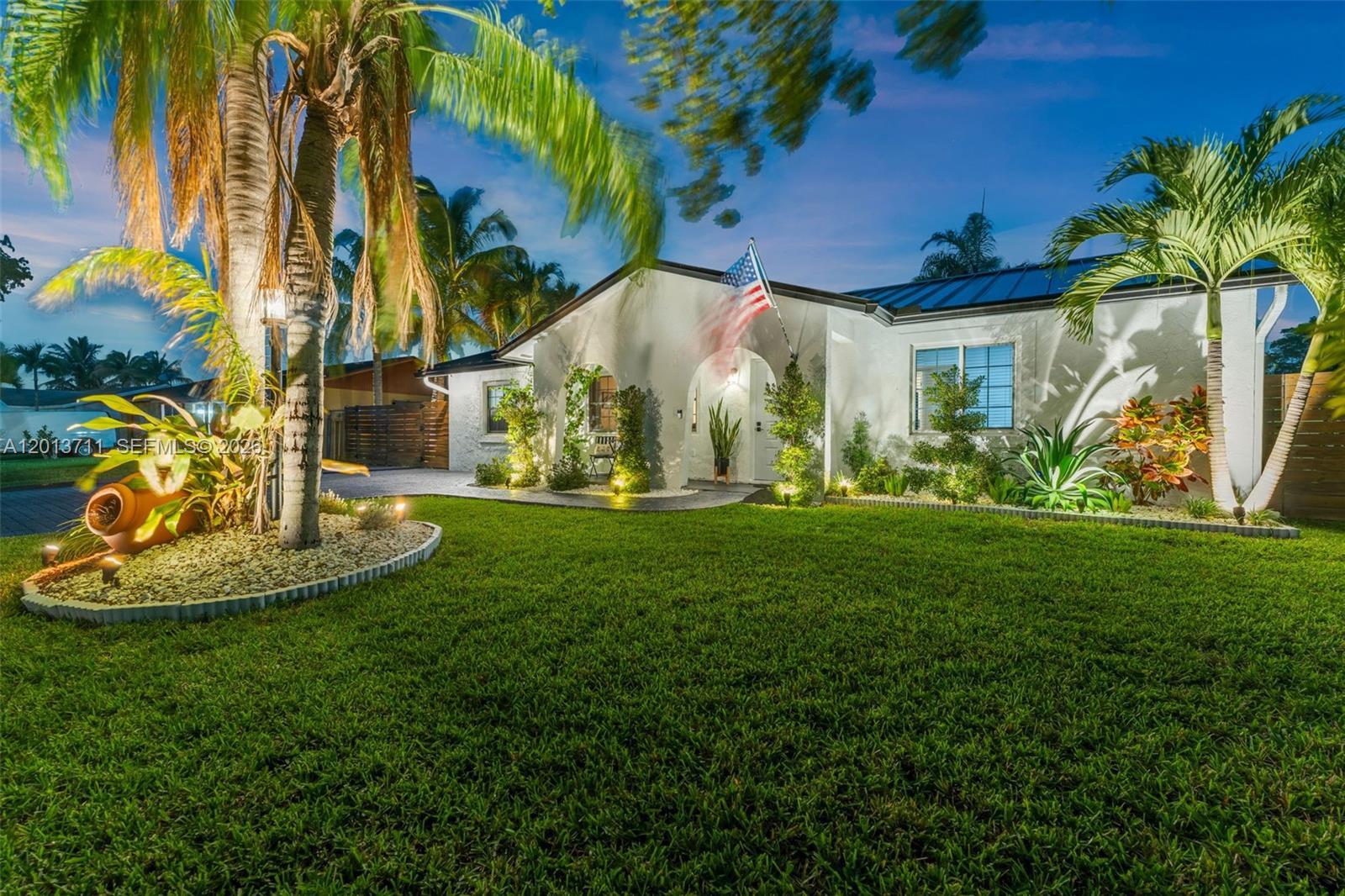 A white single-story house with a palm tree, manicured lawn, and American flag at dusk — 6651 SW 148th Court, Miami FL 33193, MIAMI, FL