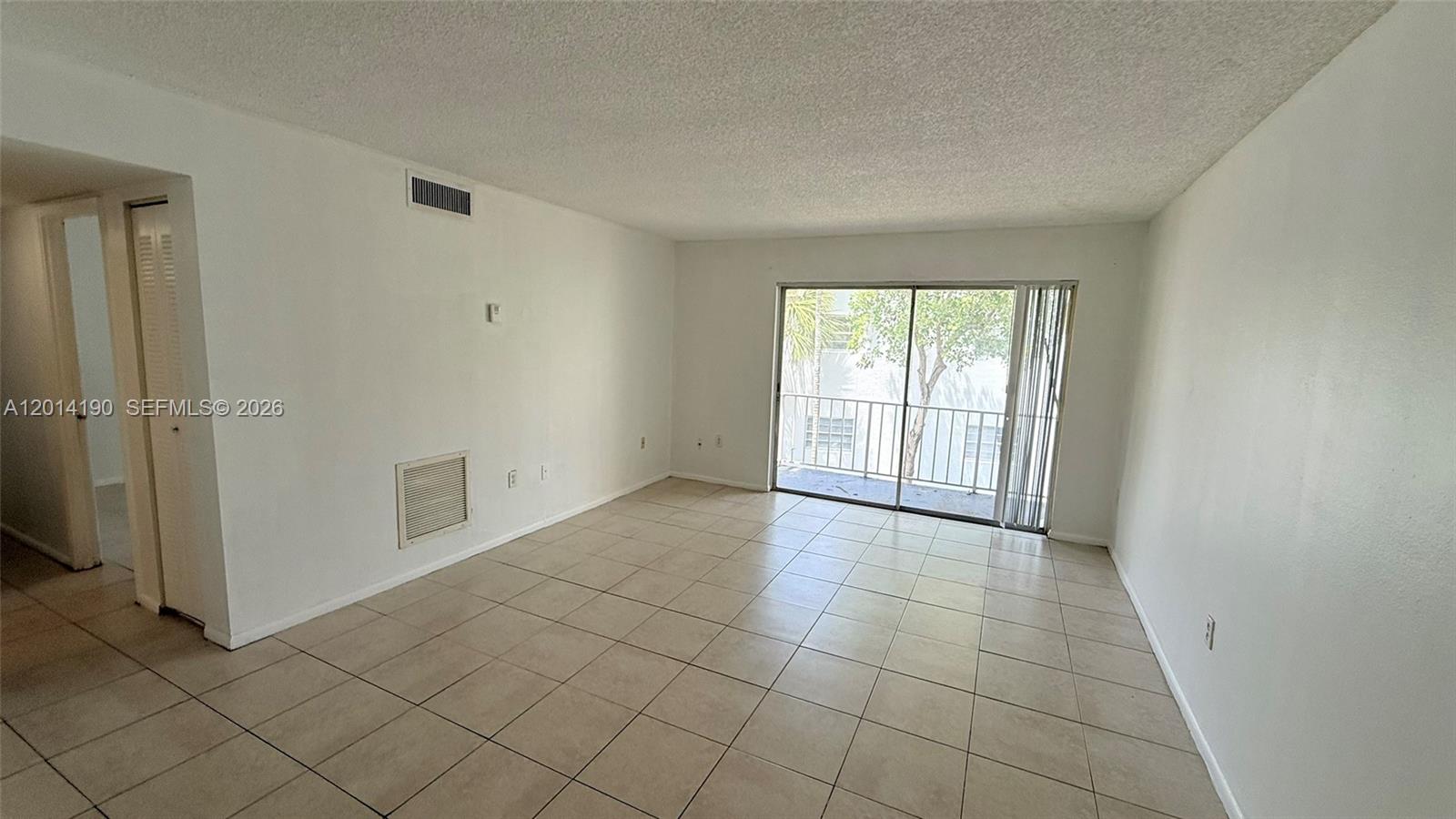 An empty room features white walls, beige tile flooring, and a sliding glass balcony door — 415 Executive Center Dr # 203, West Palm Beach FL 33401, WEST PALM BEACH, FL