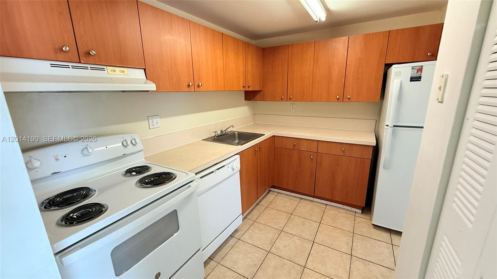 A kitchen features wood cabinets, white appliances, a tiled floor, and a laminate countertop — 415 Executive Center Dr # 203, West Palm Beach FL 33401, WEST PALM BEACH, FL