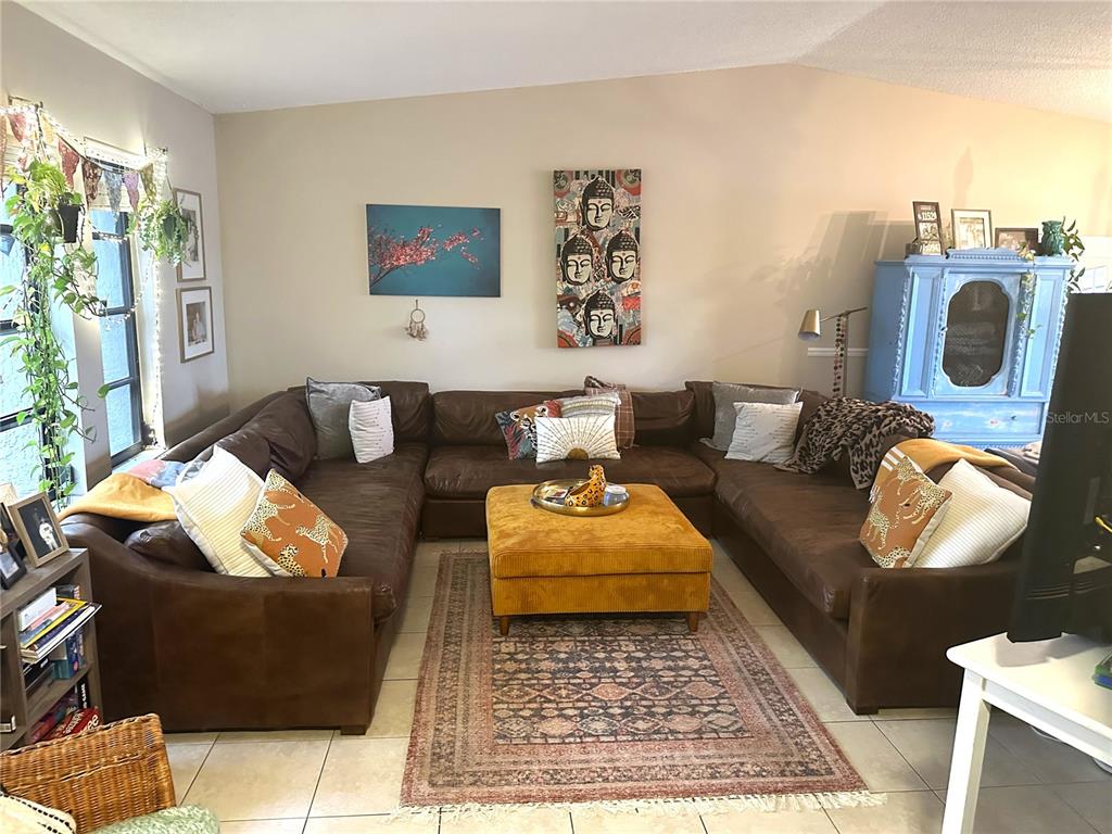 A living room features a large brown sectional sofa, a yellow ottoman, and wall art — 1170 WEXFORD DRIVE, PALM HARBOR, FL