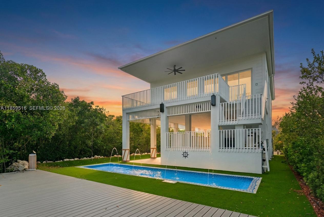A modern two-story house features a rectangular swimming pool with fountains on a grassy lawn — 862 Cardinal Ln, Key Largo FL 33037, KEY LARGO, FL