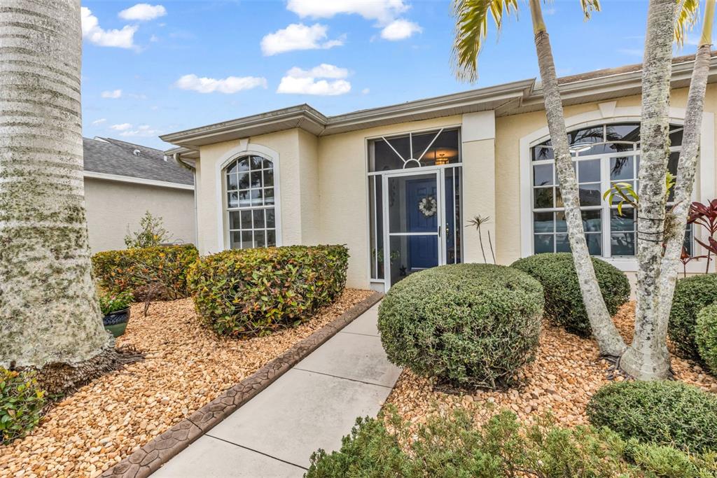A beige house exterior features a blue front door, arched windows, and a landscaped yard — 1693 PALACE COURT, PUNTA GORDA, FL