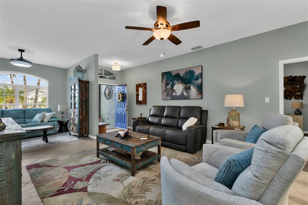 A living room features a dark leather sofa, two light gray armchairs, and a ceiling fan — 1693 PALACE COURT, PUNTA GORDA, FL