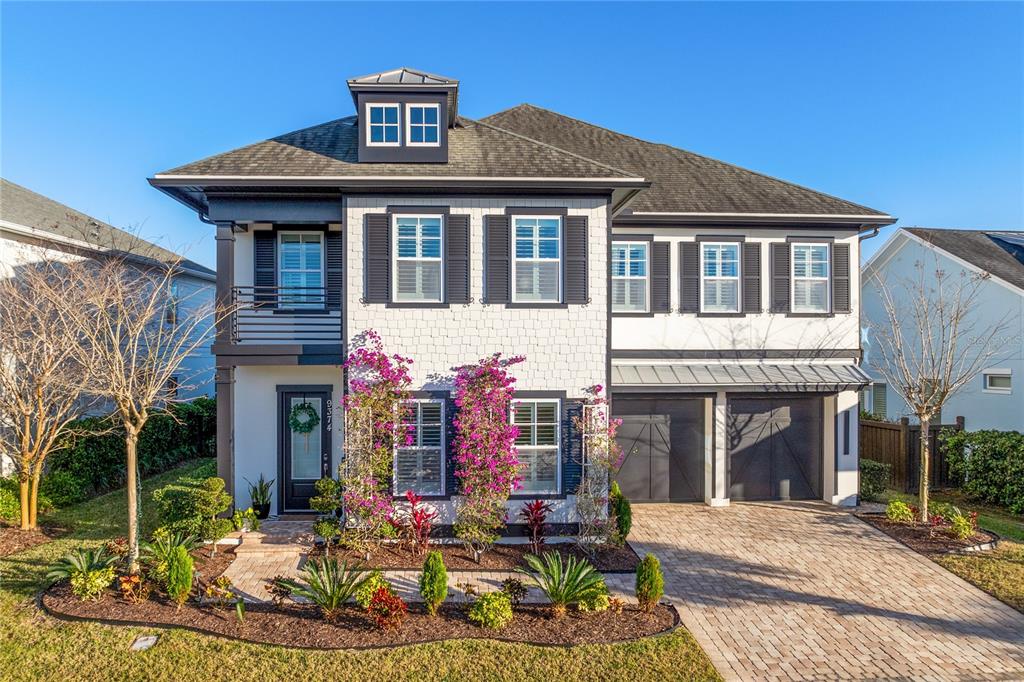 A two-story house features a white shingle facade, dark shutters, a front balcony, and a paver driveway — 9374 REYMONT STREET, ORLANDO, FL