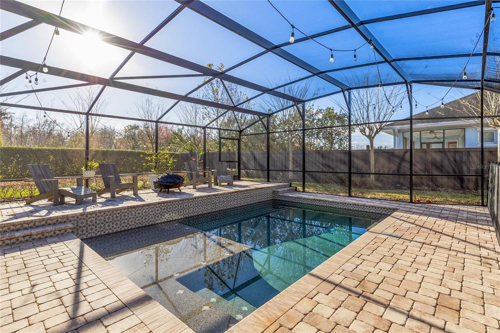 A screened-in patio features a rectangular swimming pool with decorative tile and paver decking — 9374 REYMONT STREET, ORLANDO, FL
