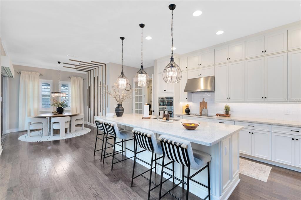 A modern kitchen features white cabinetry, a large marble island with barstools, and wood flooring — 9374 REYMONT STREET, ORLANDO, FL