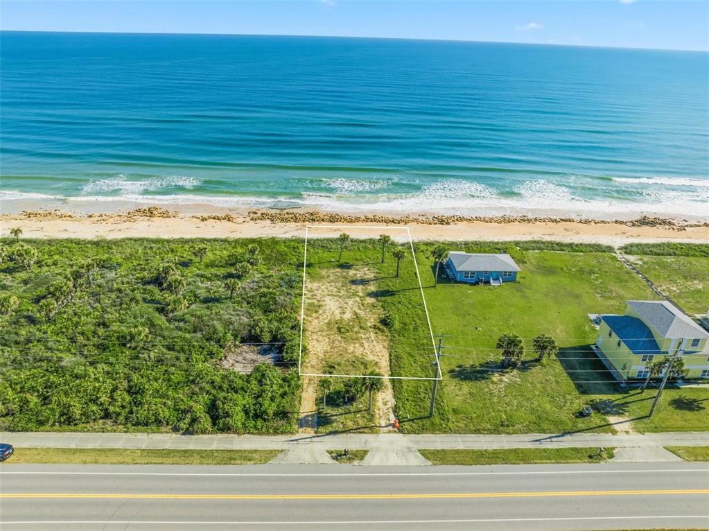 An aerial view shows a vacant oceanfront lot outlined in white between two coastal houses — 7051 N OCEAN SHORE BOULEVARD, PALM COAST, FL