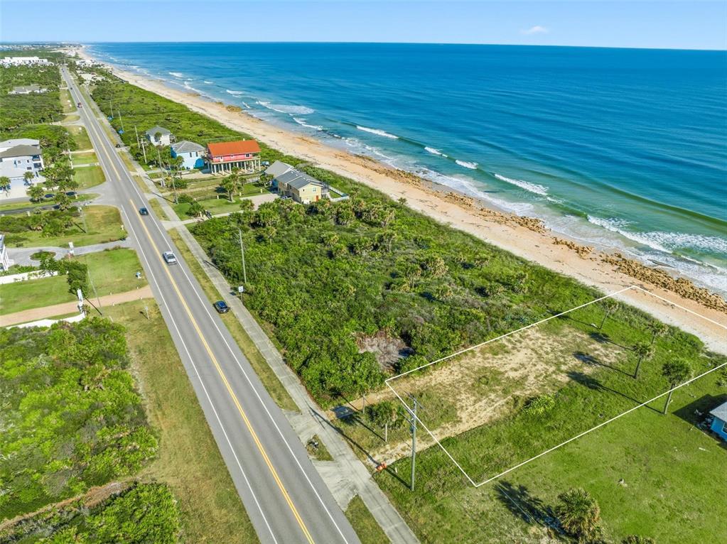 An aerial view shows a vacant coastal lot situated between a road and the ocean — 7051 N OCEAN SHORE BOULEVARD, PALM COAST, FL