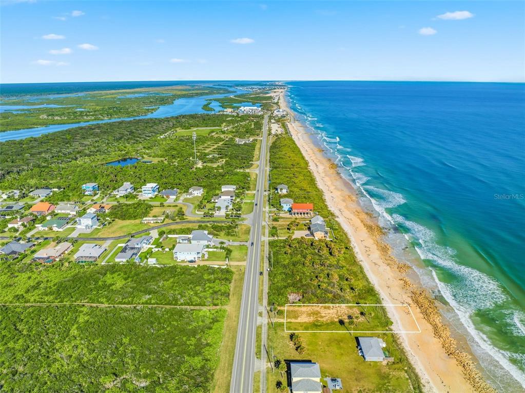 An aerial view shows a vacant oceanfront lot outlined in white along a coastal road — 7051 N OCEAN SHORE BOULEVARD, PALM COAST, FL