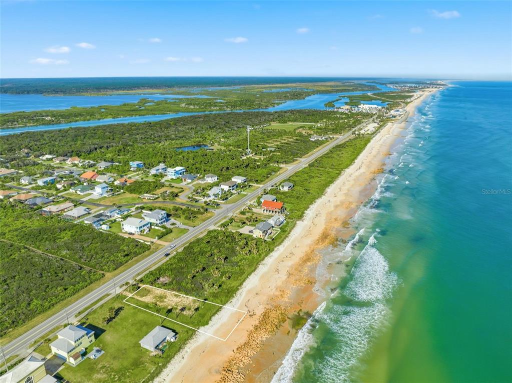An aerial view shows a vacant beachfront lot outlined in white along a coastal road — 7051 N OCEAN SHORE BOULEVARD, PALM COAST, FL