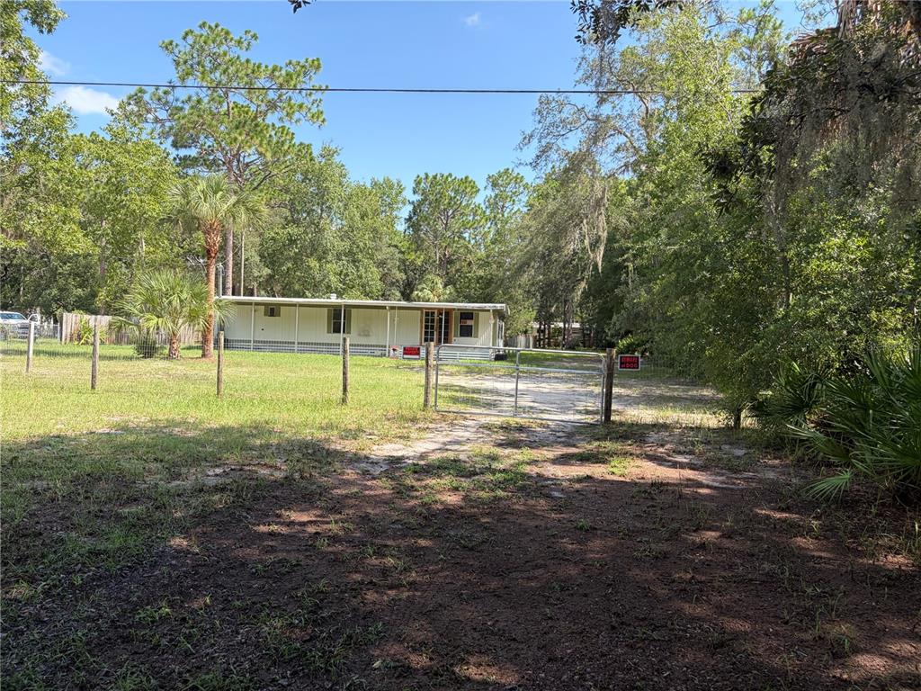 A single-story mobile home sits behind a wire fence and metal gate on a wooded lot — 6785 W COUNTRY CLUB DRIVE, HOMOSASSA, FL
