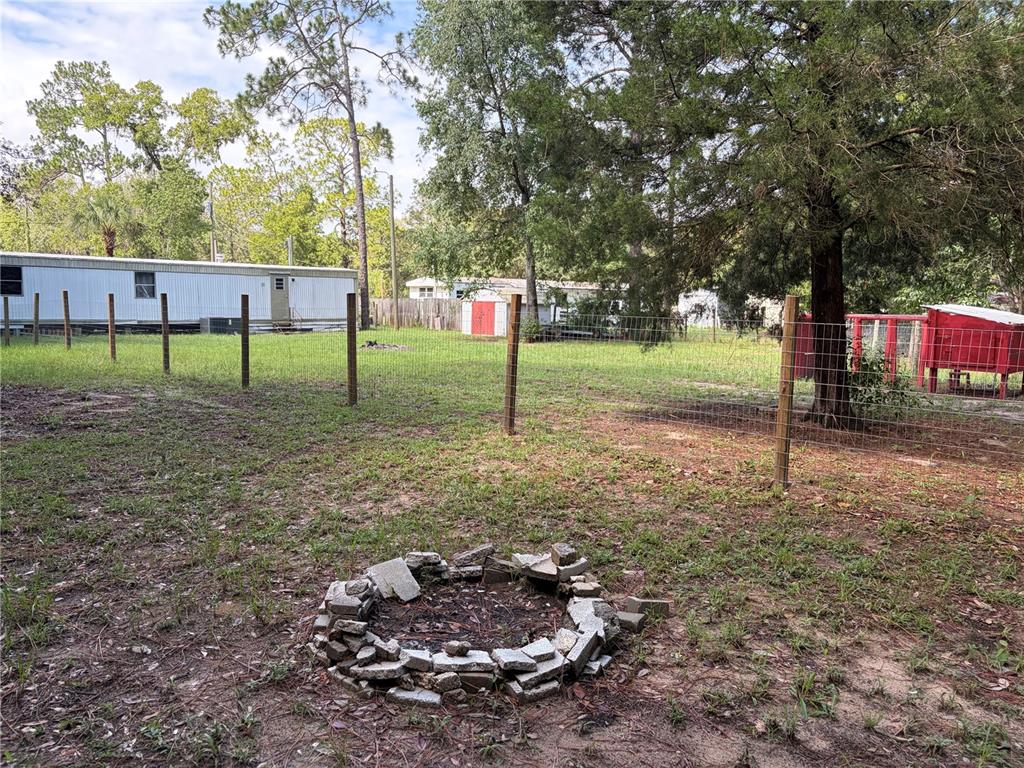 A backyard features a stone fire pit, a wire fence, and a mobile home — 6785 W COUNTRY CLUB DRIVE, HOMOSASSA, FL