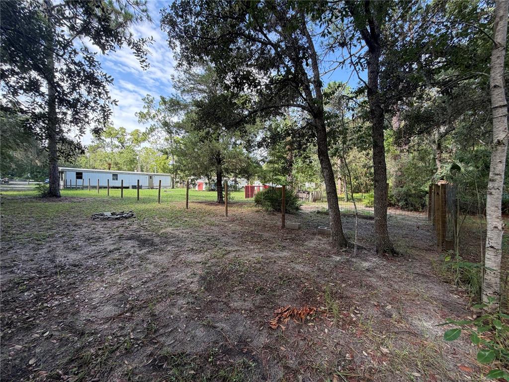 A grassy backyard features a fire pit, a wire fence, and a mobile home nearby — 6785 W COUNTRY CLUB DRIVE, HOMOSASSA, FL