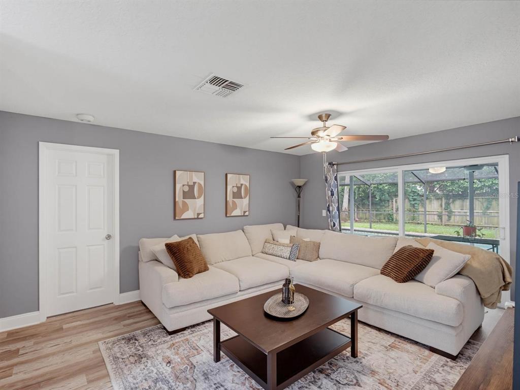 A living room features a large sectional sofa, a coffee table, and a sliding glass door — 2988 PINEWOOD RUN, PALM HARBOR, FL