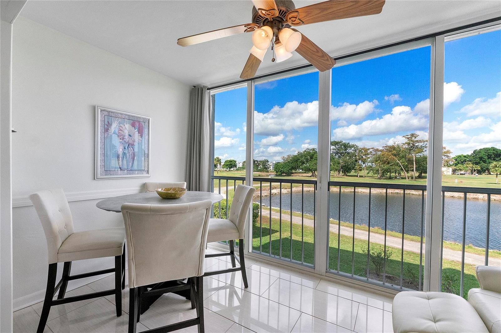 A dining area features a round table, four chairs, and floor-to-ceiling windows overlooking a lake — 7807 Golf Circle Drive # 211, Margate FL 33063, MARGATE, FL