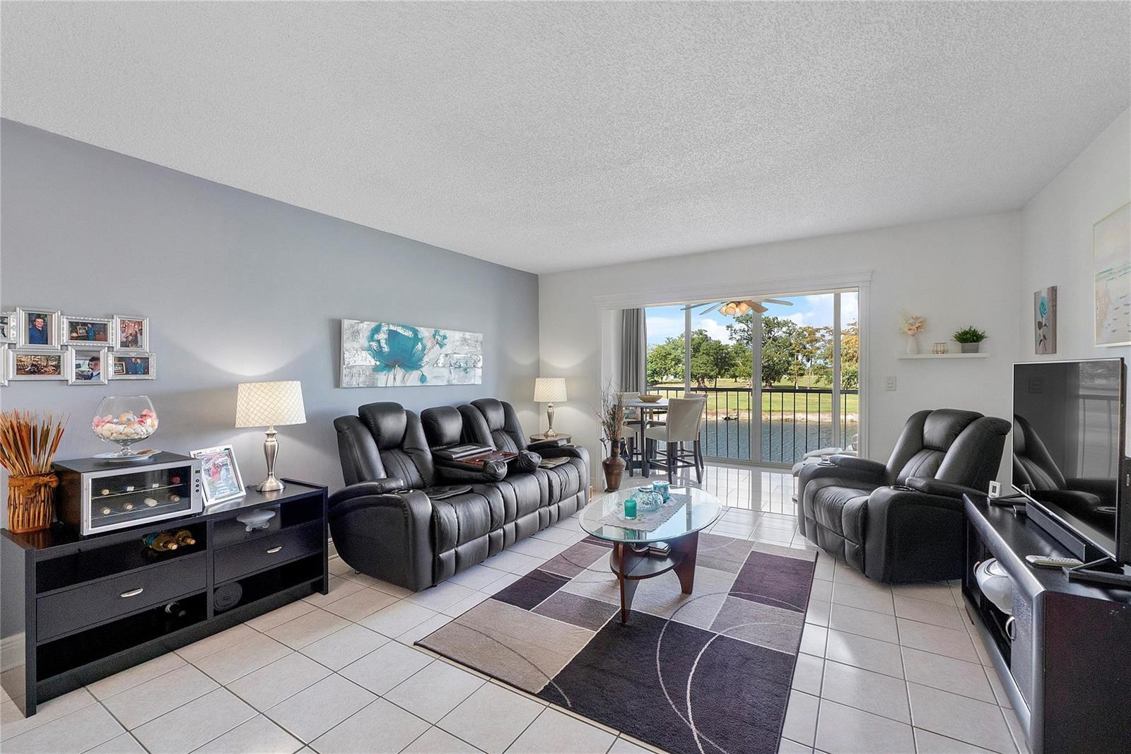 A living room features tile flooring, black leather furniture, and a sliding door to a balcony — 7807 Golf Circle Drive # 211, Margate FL 33063, MARGATE, FL