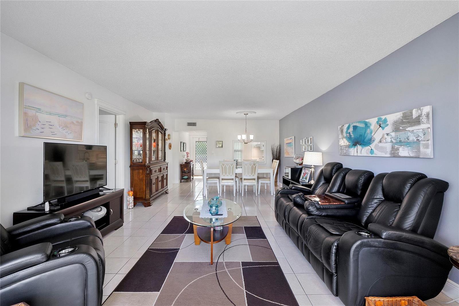 A living room with tile floors, a black leather sofa, and a dining area beyond — 7807 Golf Circle Drive # 211, Margate FL 33063, MARGATE, FL