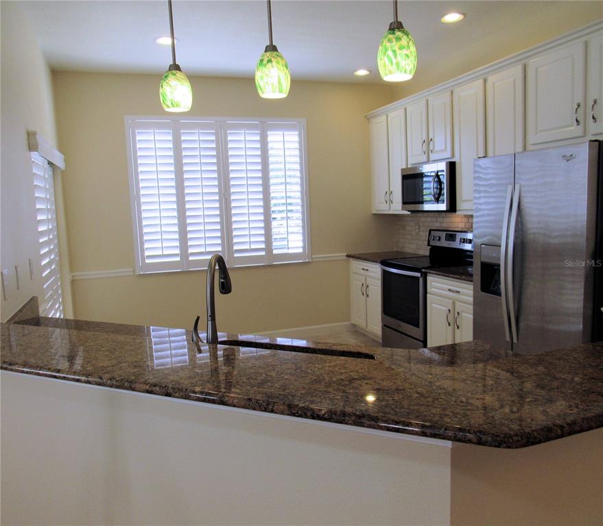 A kitchen features white cabinets, granite countertops, stainless steel appliances, and three hanging pendant lights — 4012 DEBERRY DRIVE, SARASOTA, FL