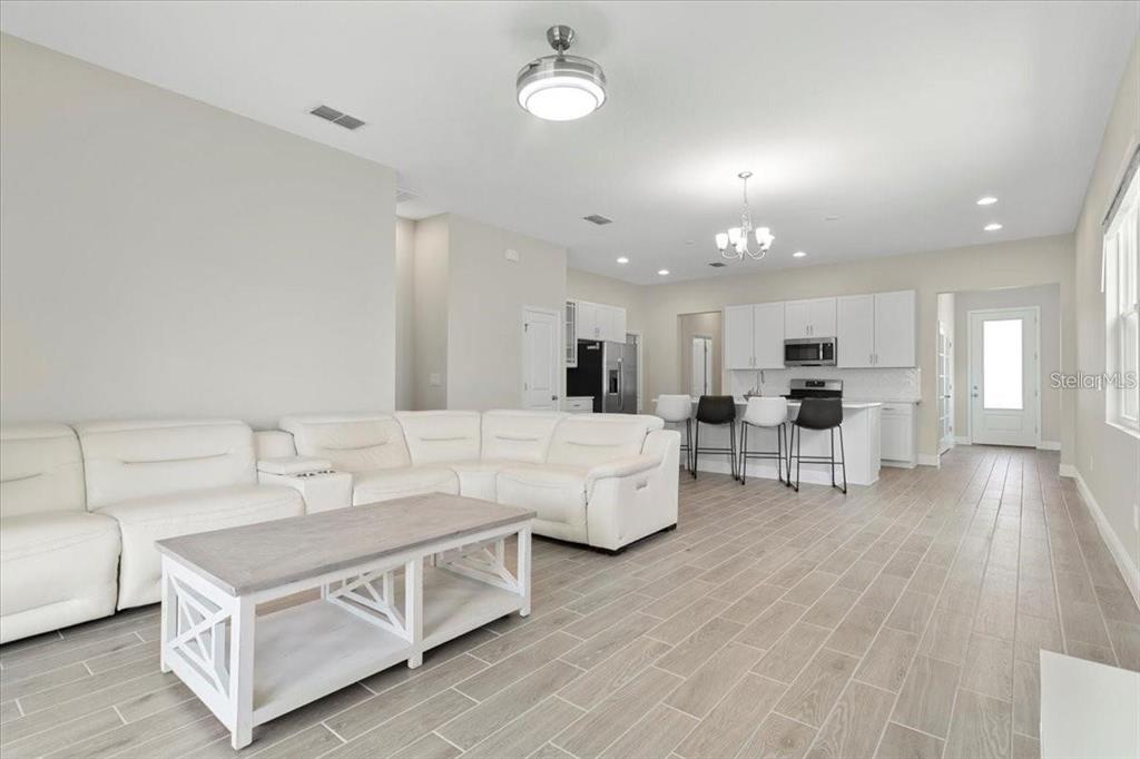 An open-concept living room features a white sectional sofa, a coffee table, and a kitchen — 1691 KEY BAY TRAIL, KISSIMMEE, FL