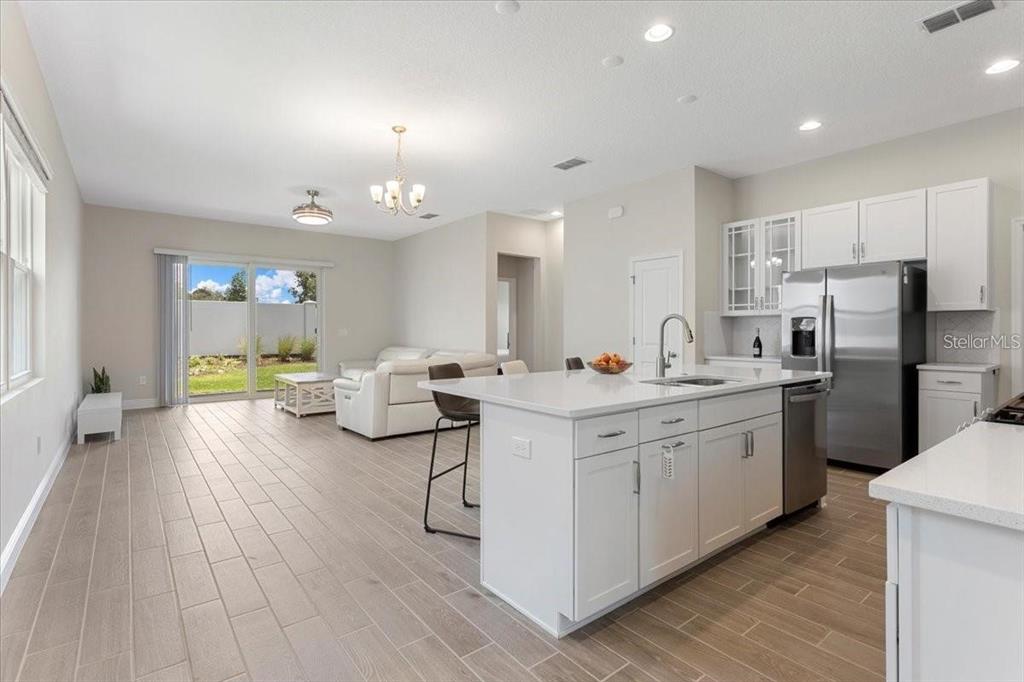 A bright, open-concept kitchen and living area features white cabinetry, a center island, and tile flooring — 1691 KEY BAY TRAIL, KISSIMMEE, FL