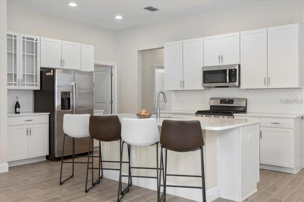 A modern kitchen features white cabinetry, stainless steel appliances, and a central island with seating — 1691 KEY BAY TRAIL, KISSIMMEE, FL