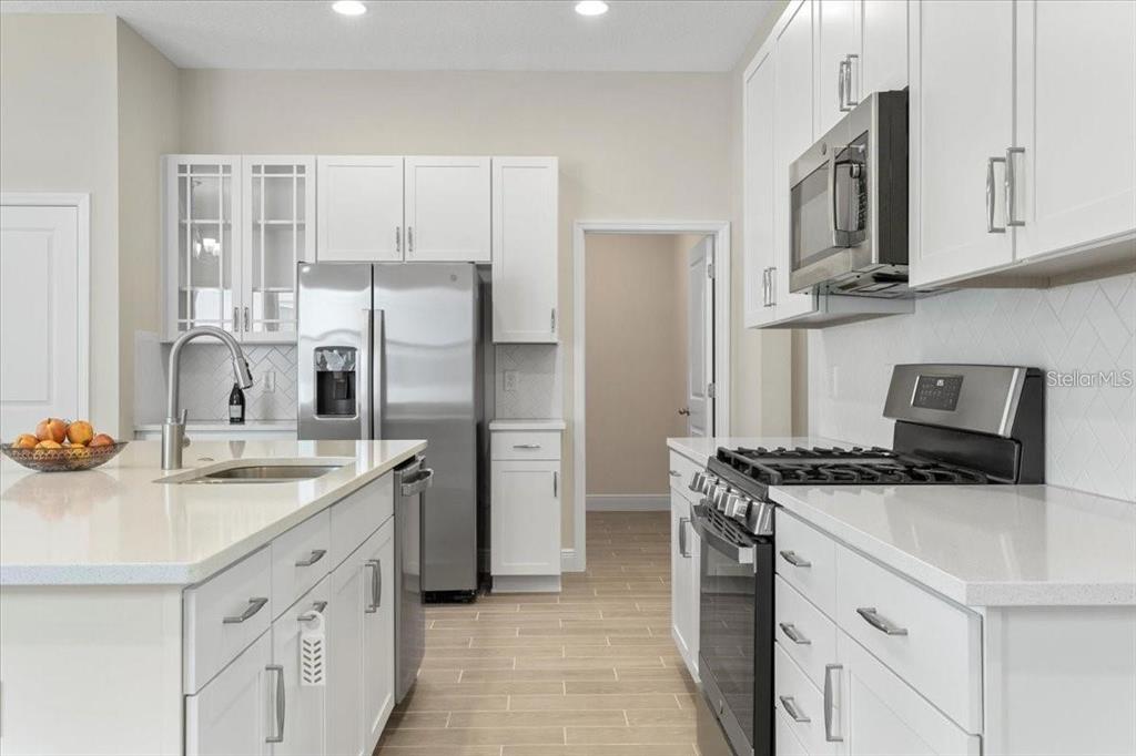 A modern kitchen features white cabinetry, stainless steel appliances, a center island, and tile flooring — 1691 KEY BAY TRAIL, KISSIMMEE, FL