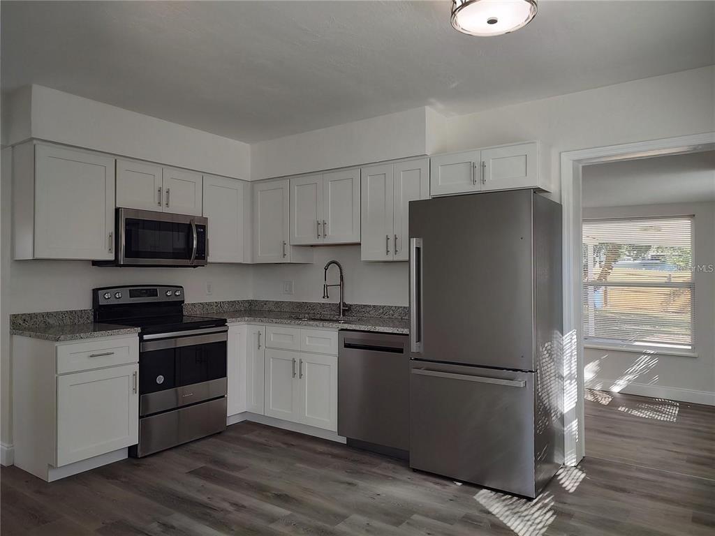 A kitchen features white cabinets, stainless steel appliances, granite countertops, and wood-look flooring — 4637 12TH AVENUE N, ST PETERSBURG, FL
