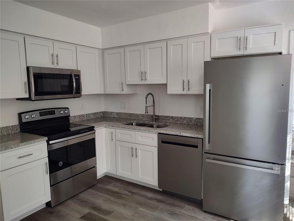 A kitchen features white cabinets, stainless steel appliances, granite countertops, and wood-look flooring — 4637 12TH AVENUE N, ST PETERSBURG, FL