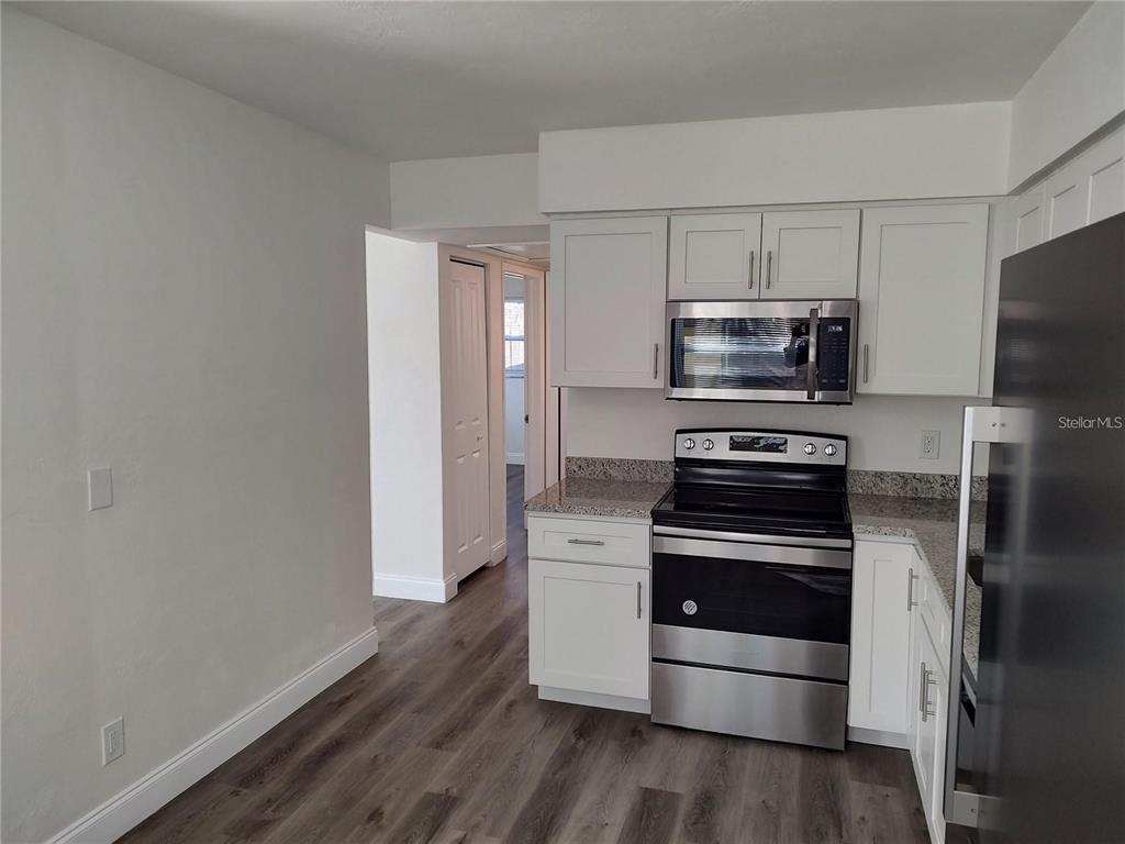 A kitchen features white cabinets, stainless steel appliances, granite countertops, and wood-look flooring — 4637 12TH AVENUE N, ST PETERSBURG, FL