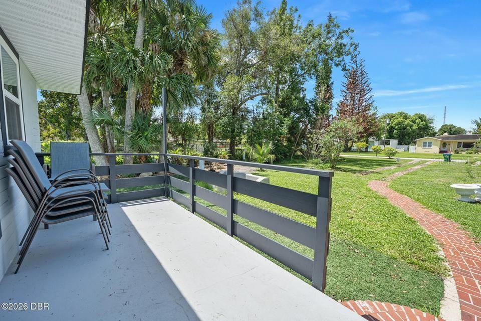 A gray porch with a wooden railing overlooks a grassy backyard with a brick path — 419 BURLEIGH AVENUE, HOLLY HILL, FL