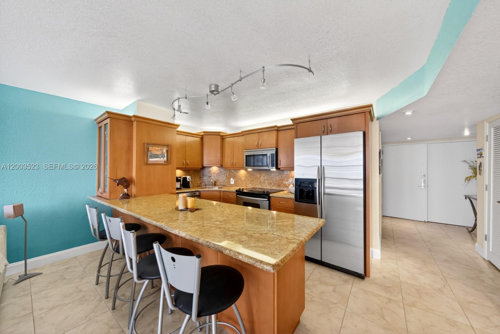 A kitchen features light wood cabinets, granite countertops, stainless steel appliances, and a breakfast bar — 6423 Collins Ave # 1204, Miami Beach FL 33141, MIAMI BEACH, FL