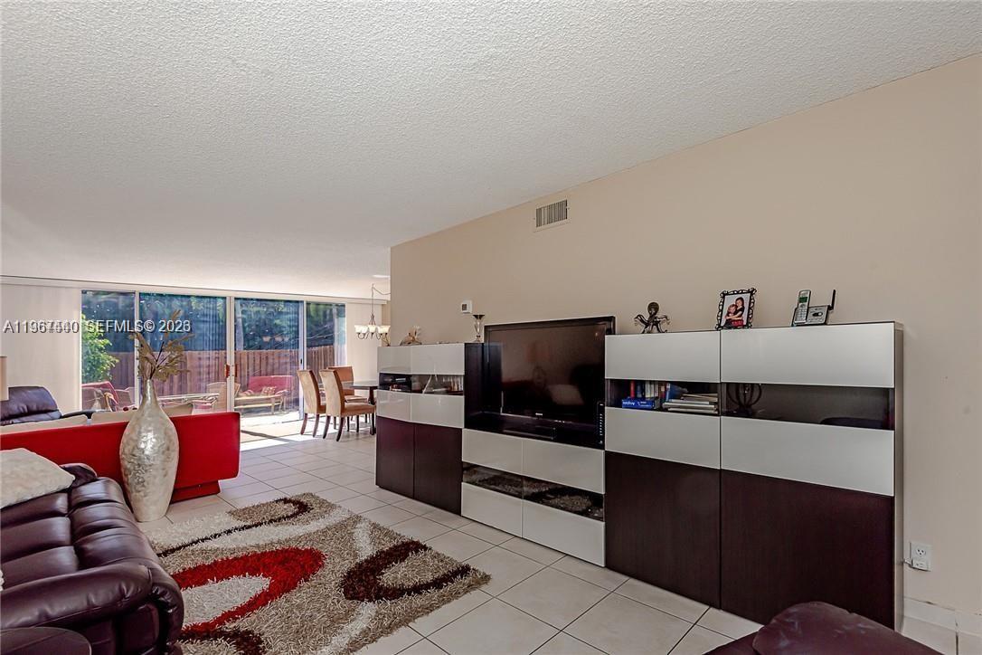 A living room features tile floors, a large media console, and a view of a patio — 2304 NE 7th St # 27, Hallandale Beach FL 33009, HALLANDALE BEACH, FL