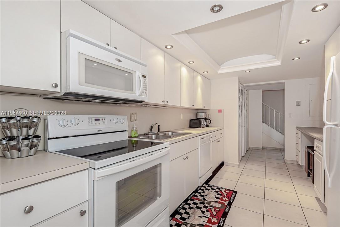 A white kitchen features white cabinets, a glass-top stove, and tiled flooring — 2304 NE 7th St # 27, Hallandale Beach FL 33009, HALLANDALE BEACH, FL