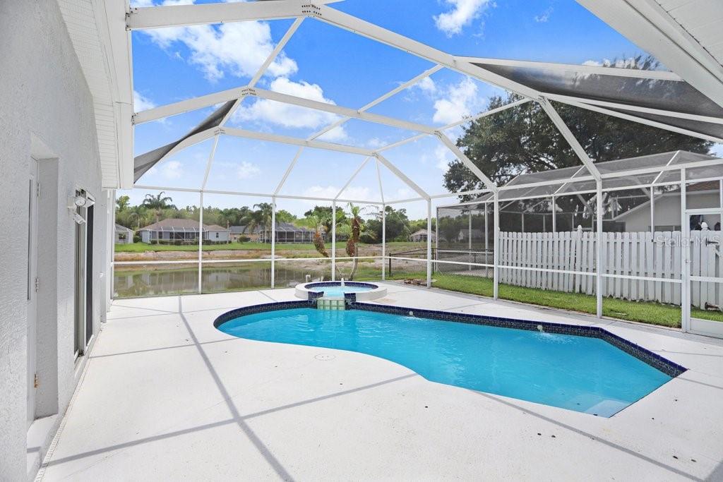 A screened-in patio features a swimming pool with an attached spa overlooking a pond — 10227 QUAILS LANDING AVENUE, TAMPA, FL
