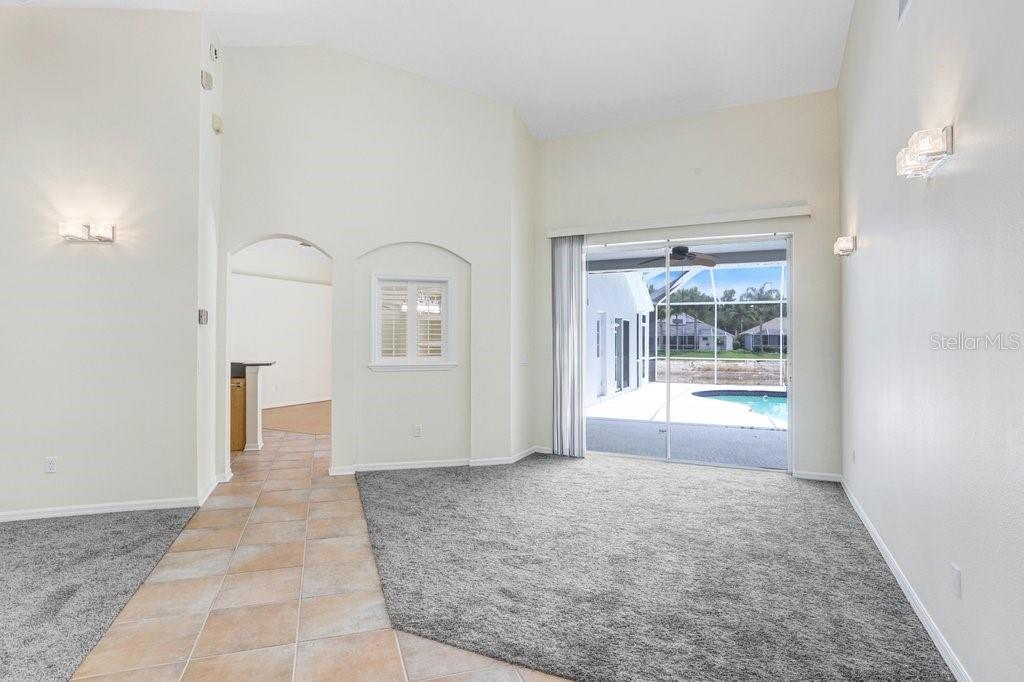 A living room with gray carpet, tile flooring, vaulted ceilings, and sliding doors to a pool — 10227 QUAILS LANDING AVENUE, TAMPA, FL