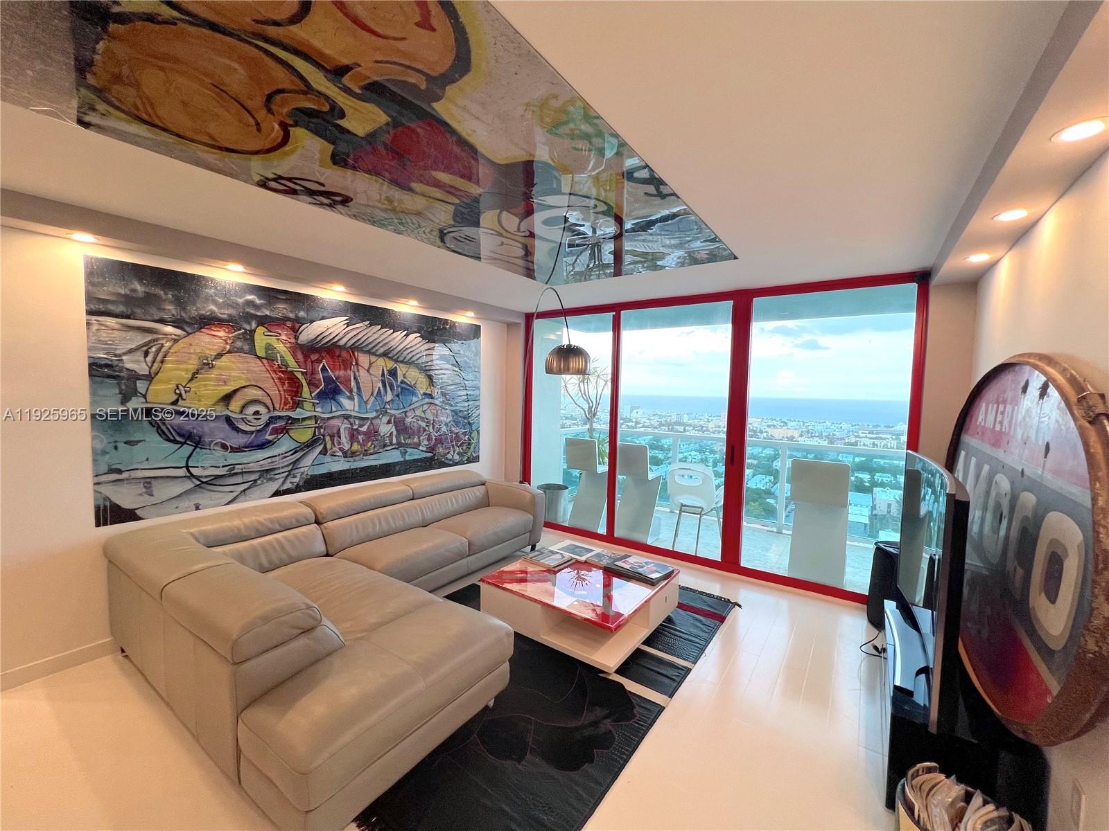 A modern living room features a large sectional sofa, graffiti-style wall and ceiling art, and balcony views — 650 West Ave # 2804, Miami Beach FL 33139, MIAMI BEACH, FL