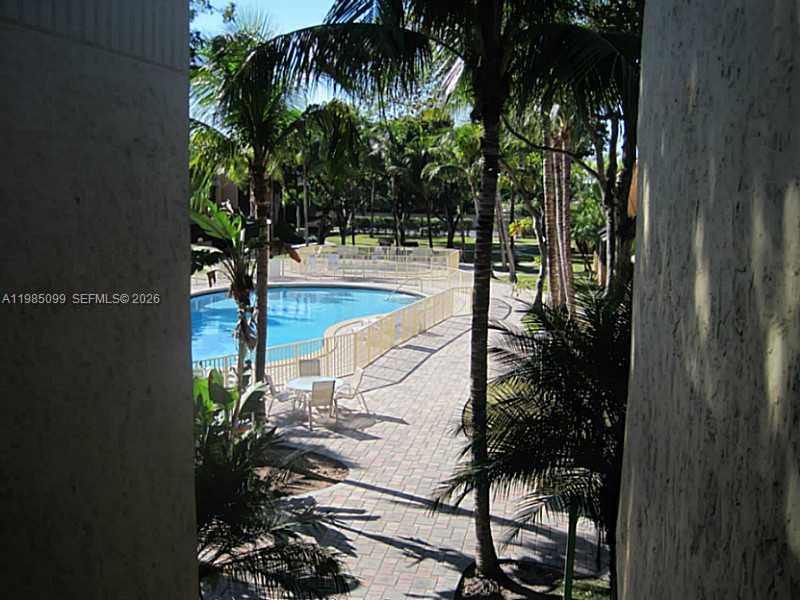 A view from a balcony overlooking a swimming pool surrounded by palm trees and pavers — 7913 SW 104th St # G, Miami FL 33156, MIAMI, FL